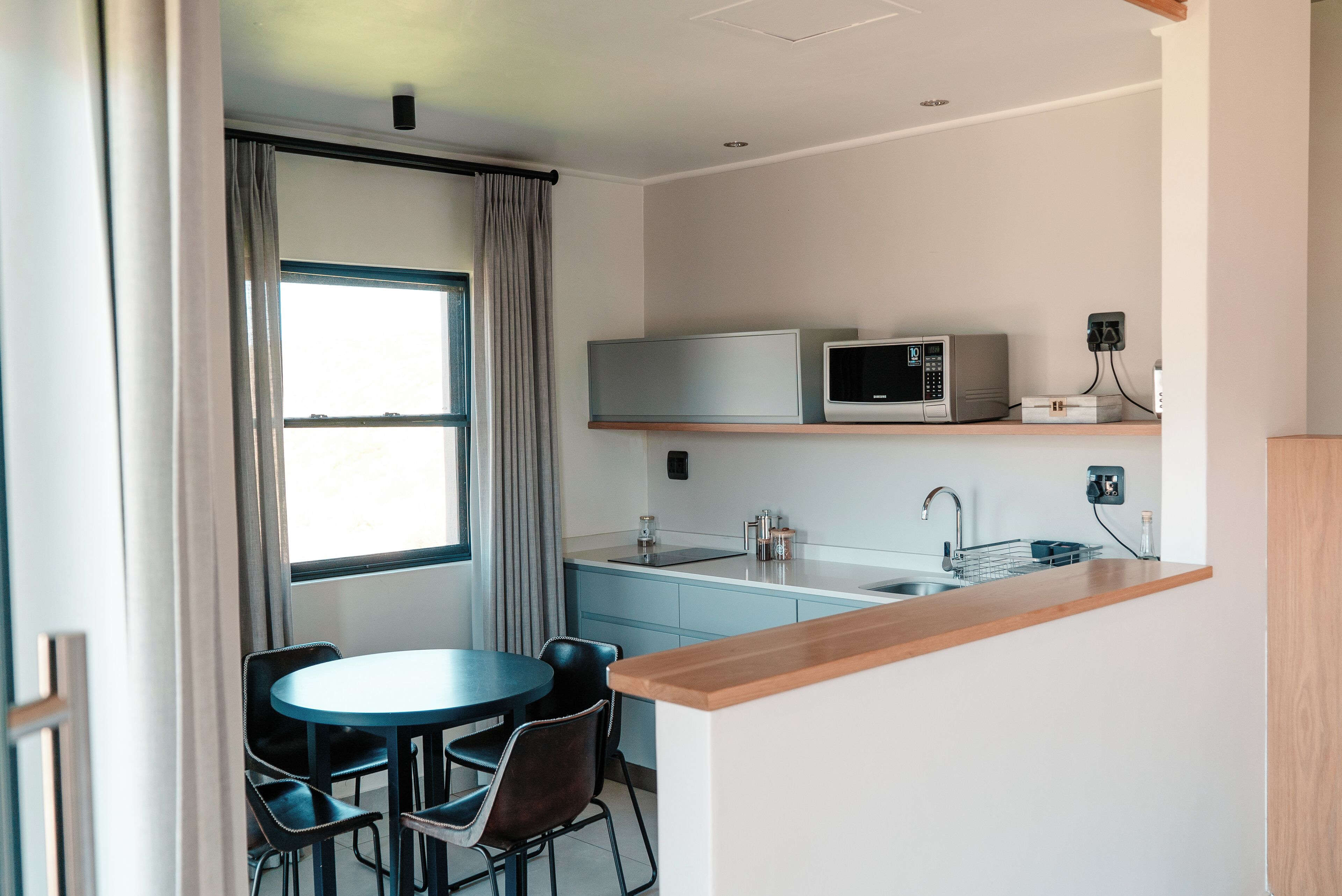 A compact kitchen with a microwave, a small refrigerator, a sink, and a dining area with a table and chairs.