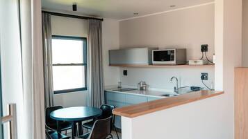 Cocina compacta equipada con microondas, un refrigerador pequeño, un lavamanos y una zona de comedor con mesa y sillas.