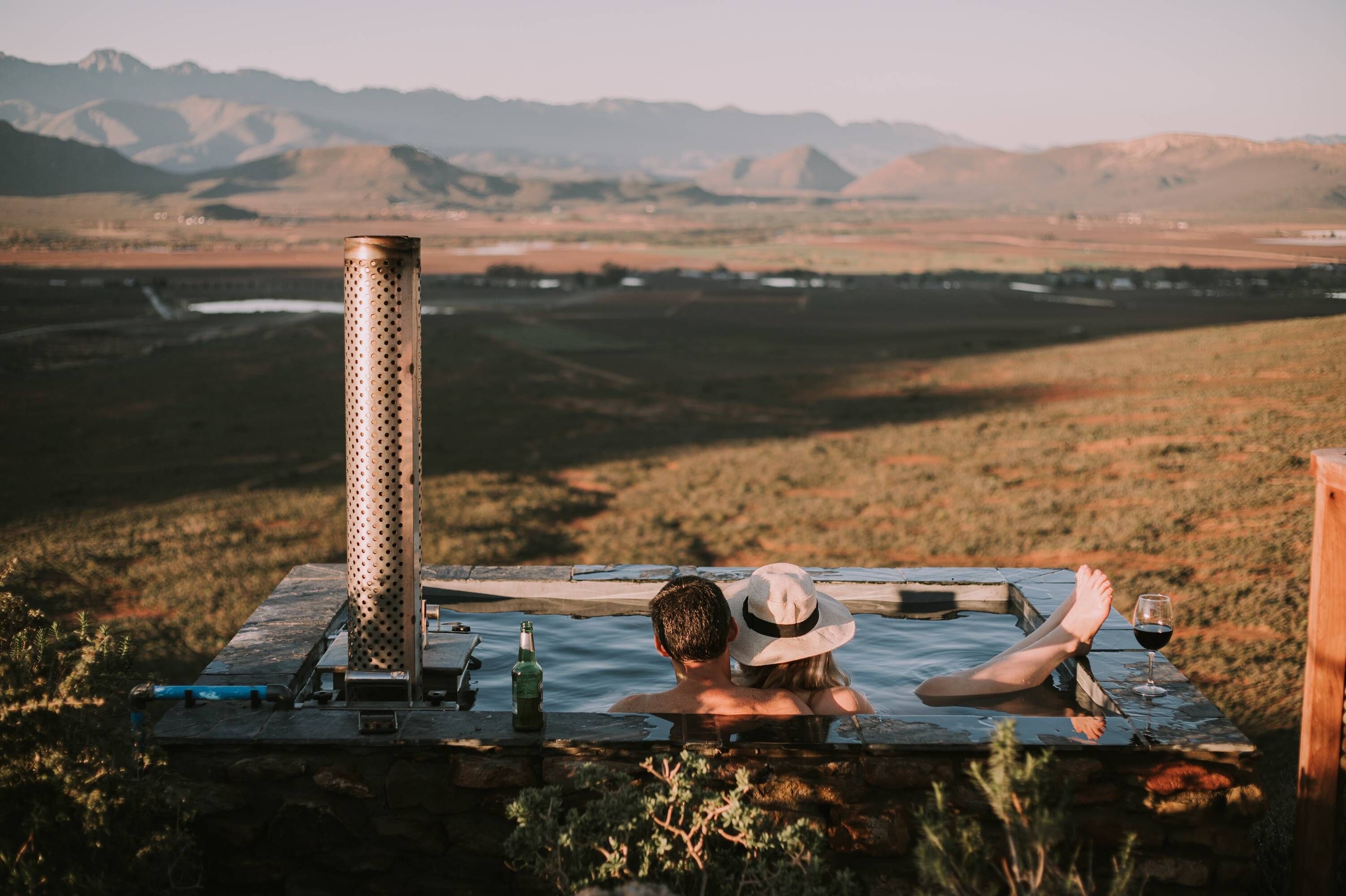 Una pareja relajándose en un jacuzzi con vistas a la montaña, una botella y una copa de vino.