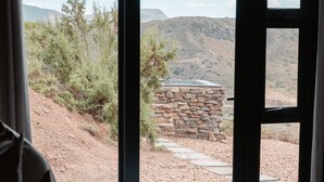Un dormitorio con un amplio ventanal que da a un paisaje desértico, una pared de piedra y una chimenea de piedra.
