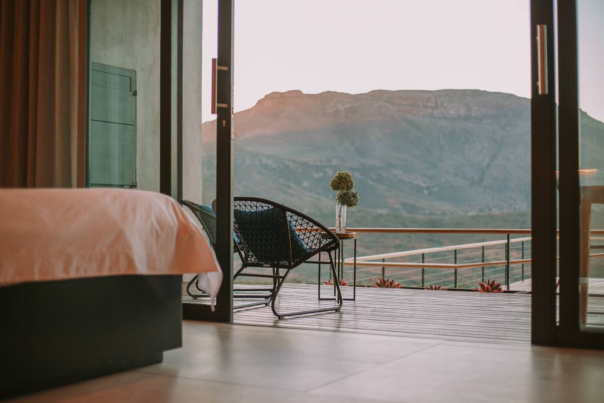 A bedroom with a bed, a chair, and a view of mountains through an open door.