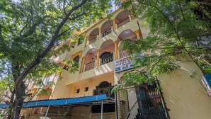 A multi-story building with balconies, a sign for a hotel, and surrounding greenery. - iROOMZ Hotel Ritzy Grand (Hyderabad)
