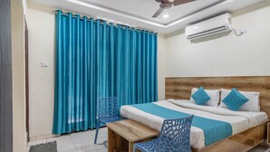 A bedroom with a wooden bed, blue chairs, a ceiling fan, and an air conditioning unit. - iROOMZ Hotel Ritzy Grand (Hyderabad)