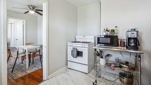Une cuisine compacte équipée d’une cuisinière blanche, d’un four à micro-ondes et d’une machine à café, ainsi que d’un petit coin repas avec une table et des chaises, et d’un ventilateur de plafond.