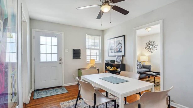 Un coin repas avec une table blanche, quatre chaises, un ventilateur de plafond et un tapis.