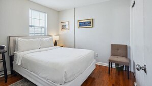 Une chambre à coucher comprenant un lit, une chaise, une table de chevet, une lampe et deux tableaux encadrés accrochés au mur.