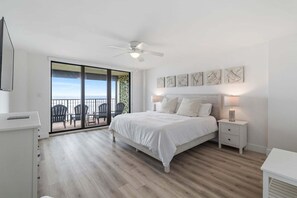 A bedroom with a bed, bedside tables, a ceiling fan, and a view of the ocean through a sliding door. - Sand Dollar 206 Ocean View (St. Augustine)