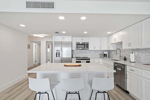 Une cuisine moderne avec des meubles blancs, des appareils en acier inoxydable et un îlot central doté de tabourets de bar.