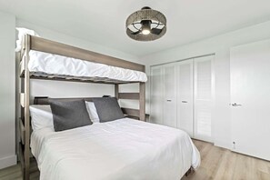 A bunk bed with white bedding and grey pillows, a ceiling light fixture, and white louvered closets. - Sand Dollar 206 Ocean View (St. Augustine)