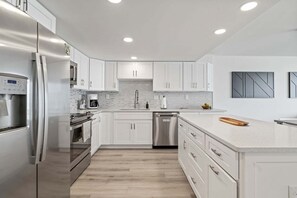 A modern kitchen with stainless steel appliances, white cabinetry, and a central island. - Sand Dollar 206 Ocean View (St. Augustine)