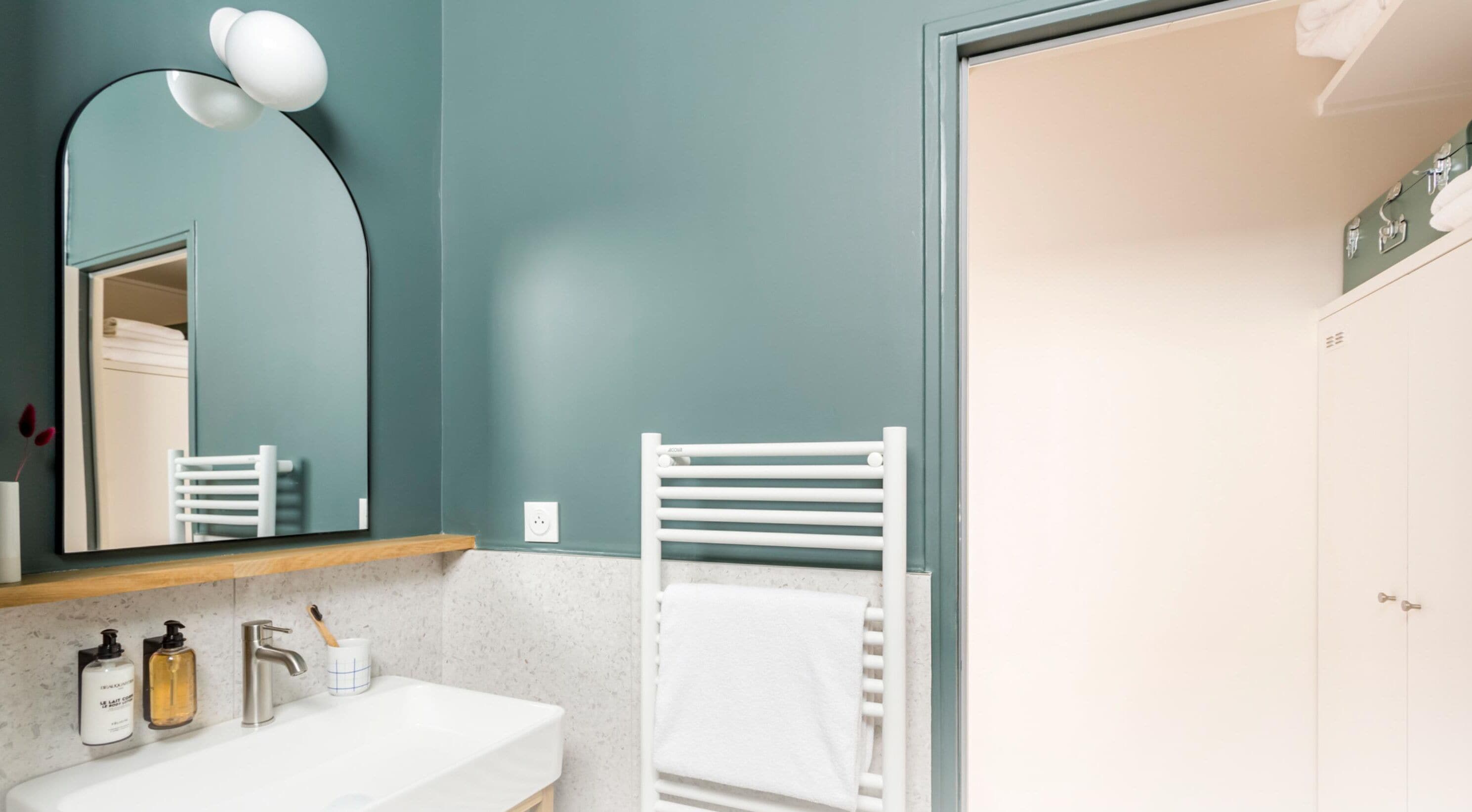 A modern bathroom with a white sink, a mirror, a towel rack, and a door.