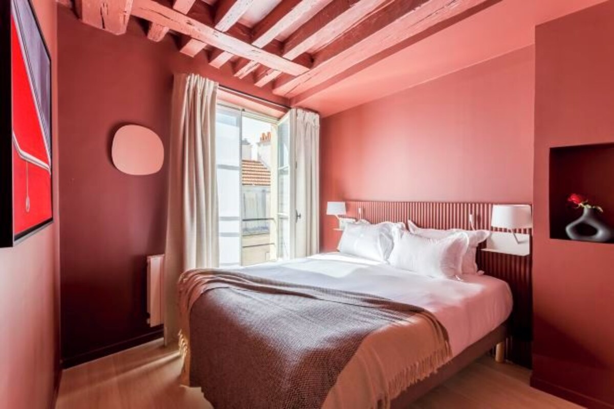Une chambre avec un grand lit, une fenêtre avec des rideaux, un élément de décoration circulaire au mur et une table de chevet avec une lampe.