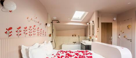 A bedroom with a bed, a skylight, a shower, and a bathroom with a sink and mirror.
