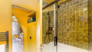 A modern bathroom with a glass shower enclosure, yellow walls, and a visible staircase leading to another room. - Beauquartier - Marais Bourg Tibourg (Paris)