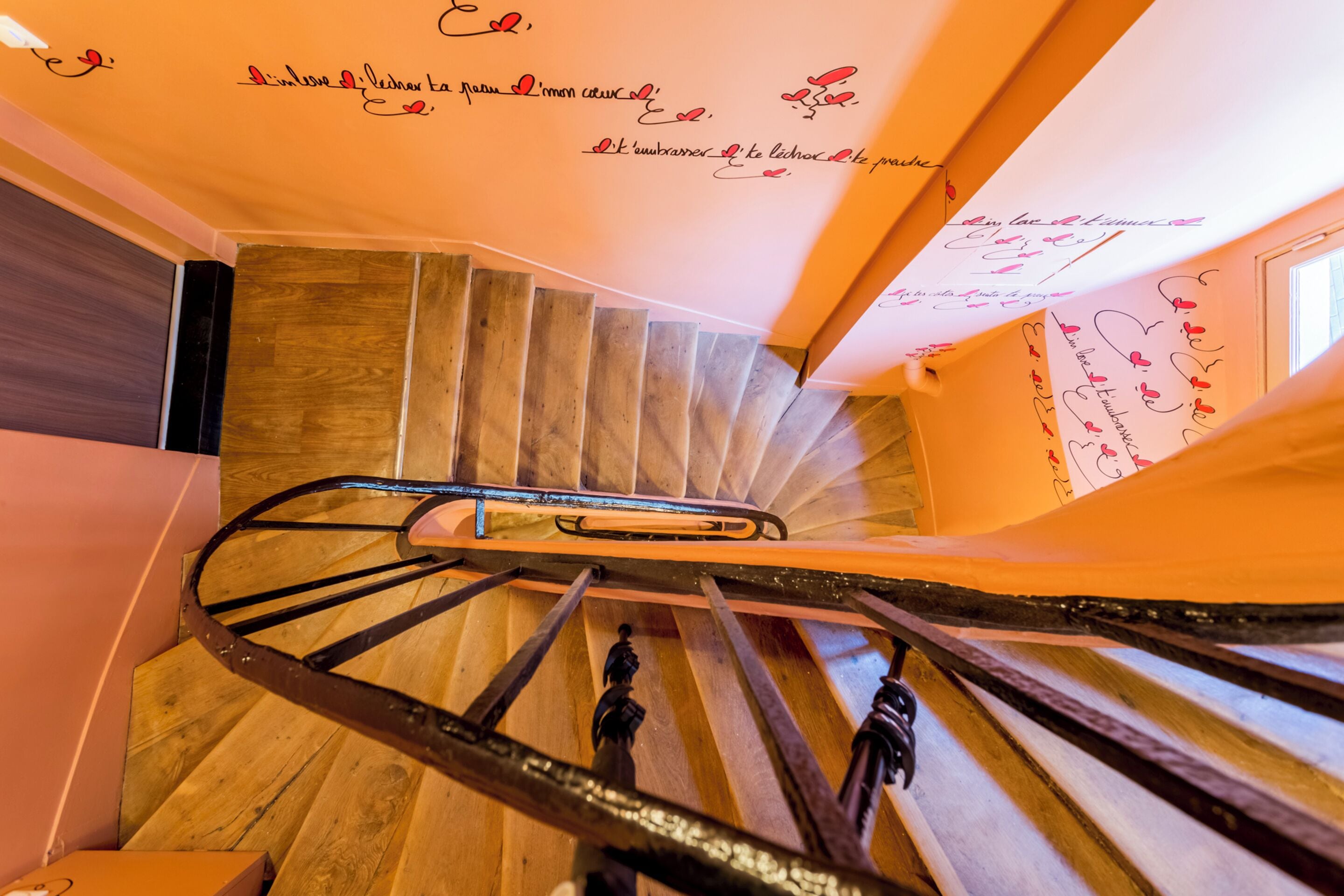 Una escalera de madera con barandas de metal y detalles decorativos en la pared.