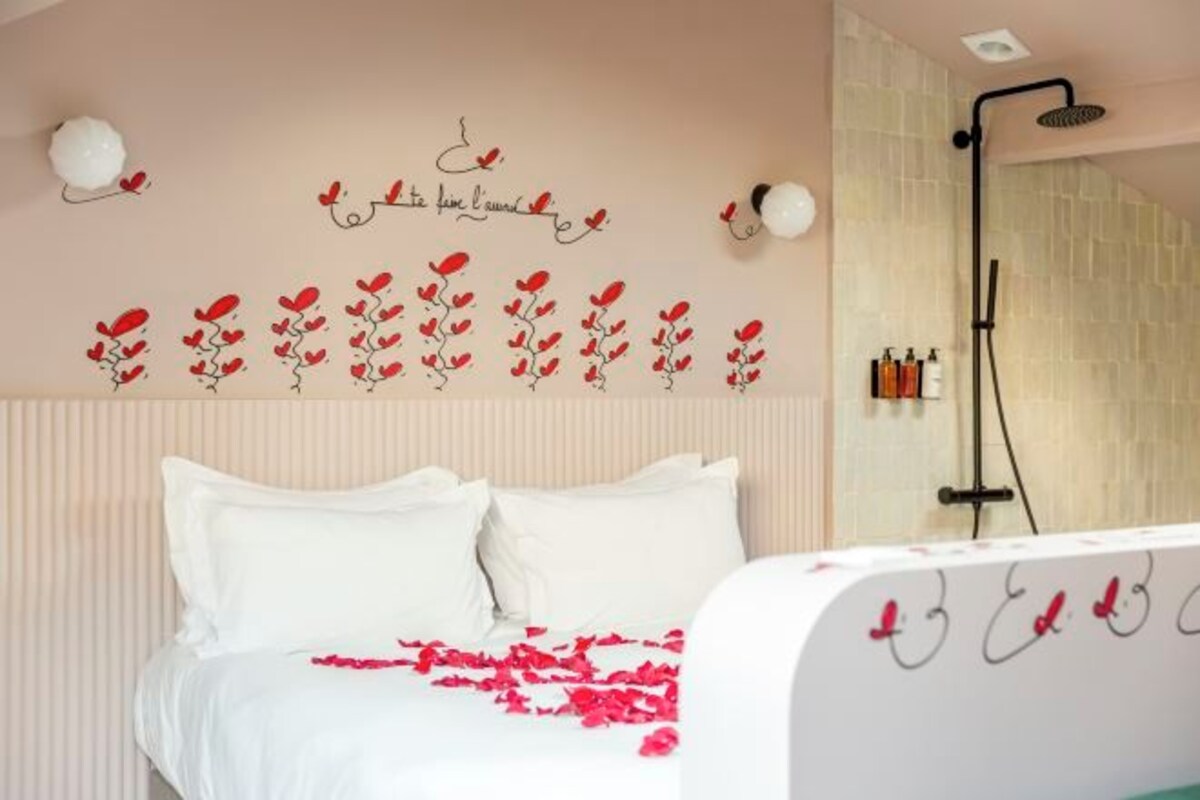 Une chambre avec un lit, un mur décoré de motifs floraux rouges, une douche et des articles de toilette rangés sur une étagère.