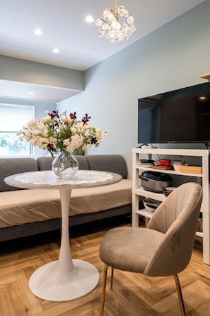 A modern living room with a round white table, a beige armchair, a grey sofa, a flat-screen TV on a white stand, and a chandelier. - NEW to our lineup 🎁 Welcome gift | We look forward to your feedback, Akasaka Premier (港区)