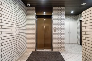 Elevador moderno em corredor com paredes de tijolo branco e carpete estampado.