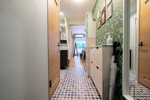Um corredor estreito com piso estampado, uma porta de madeira à direita e parede verde com padrão.