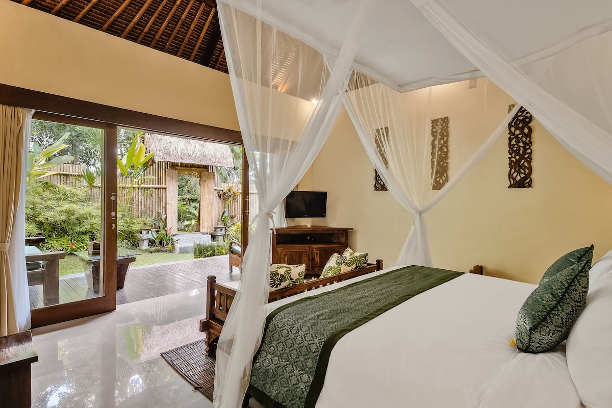 A bedroom with a bed, a TV, a wooden cabinet, and a view of a garden through a glass door.