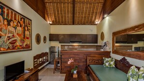 Un vaste espace de vie doté d’un plafond en bois, d’un grand tableau, d’un téléviseur, d’un canapé avec des coussins verts et d’un mur en briques.