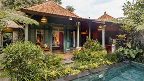 Une maison traditionnelle avec un toit en tuiles, une véranda et une piscine entourée d’une végétation luxuriante.