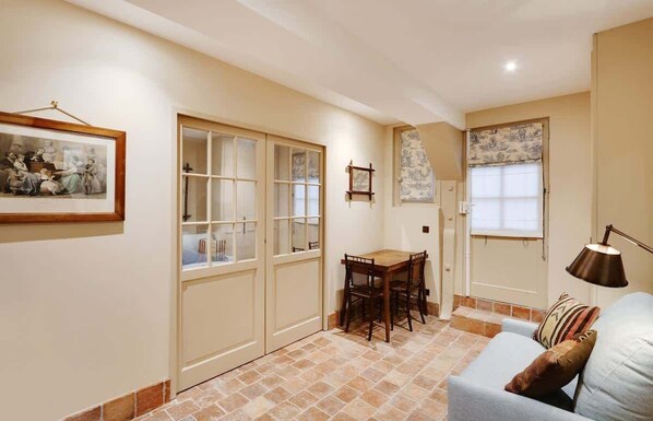 A room with a dining table and chairs, a sofa, a lamp, and a framed picture on the wall.