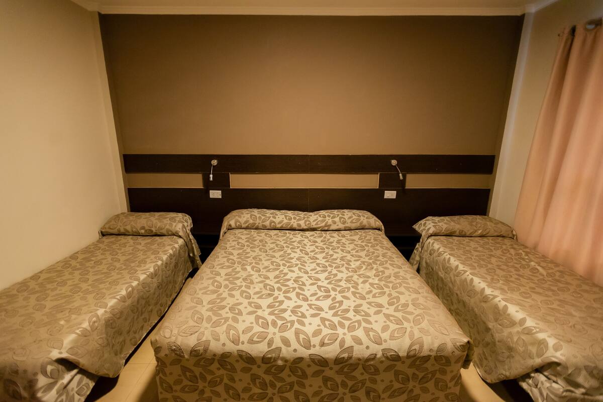 A room with three single beds aligned against a wall, each with a headboard and a bedside table.