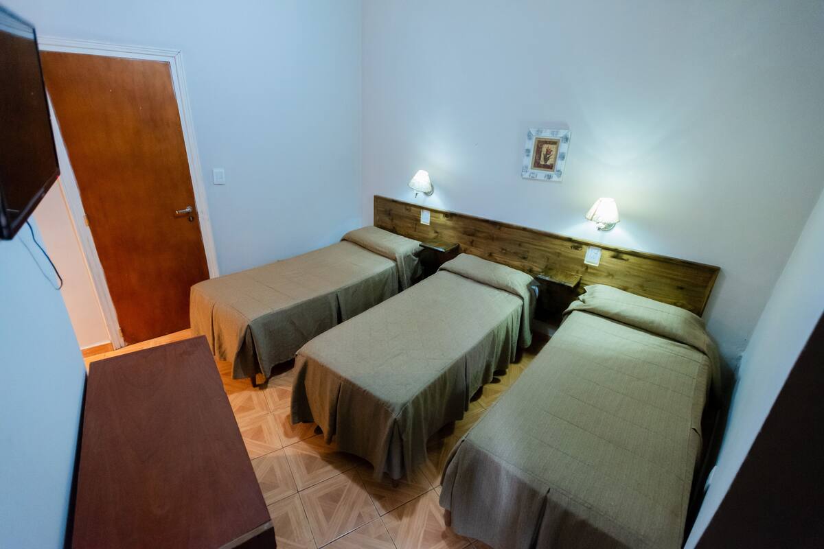 A room with four single beds, a wooden headboard, two wall-mounted lamps, and a door.