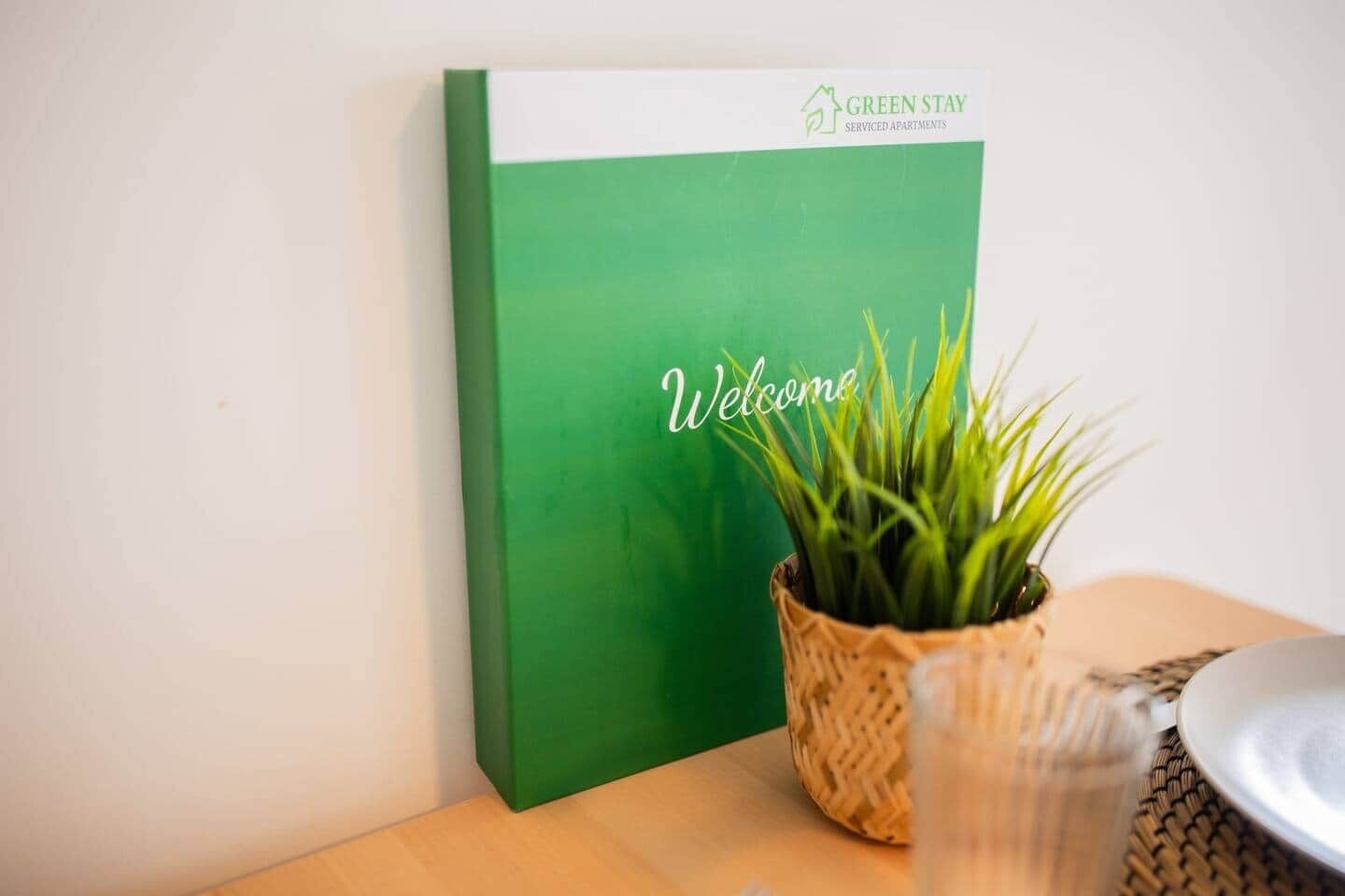 Un letrero verde con la palabra 'Welcome', colocado junto a una cesta tejida con plantas verdes.