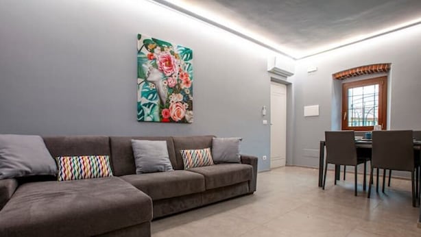 Een woonkamer met een bank, een eettafel met stoelen, en een kleurrijk schilderij aan de muur.