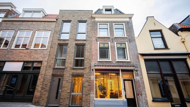 Une rangée de maisons de ville à trois étages, avec des façades en briques, de grandes fenêtres et un commerce situé au rez-de-chaussée.