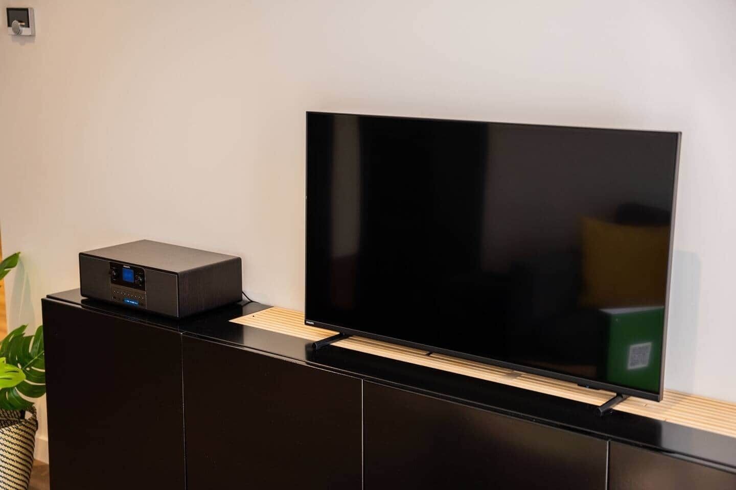 Un televisor de pantalla plana sobre un mueble negro para entretenimiento, con un pequeño dispositivo electrónico encima.