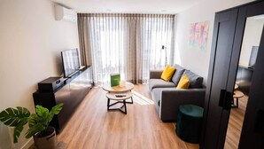 Un salon moderne avec un téléviseur à écran plat, un canapé avec des coussins jaunes, une table basse ronde et une plante en pot.