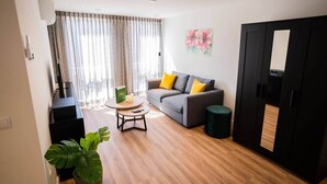 Un salon moderne avec un canapé gris, une table basse ronde et une grande fenêtre avec des rideaux.