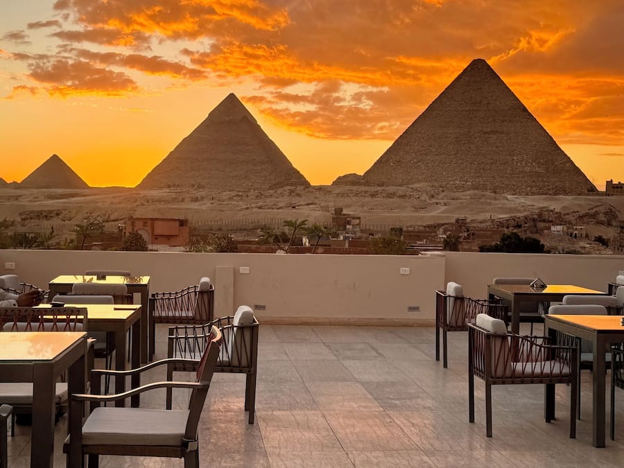 Um terraço com mesas e cadeiras, com vista para pirâmides e uma paisagem desértica.