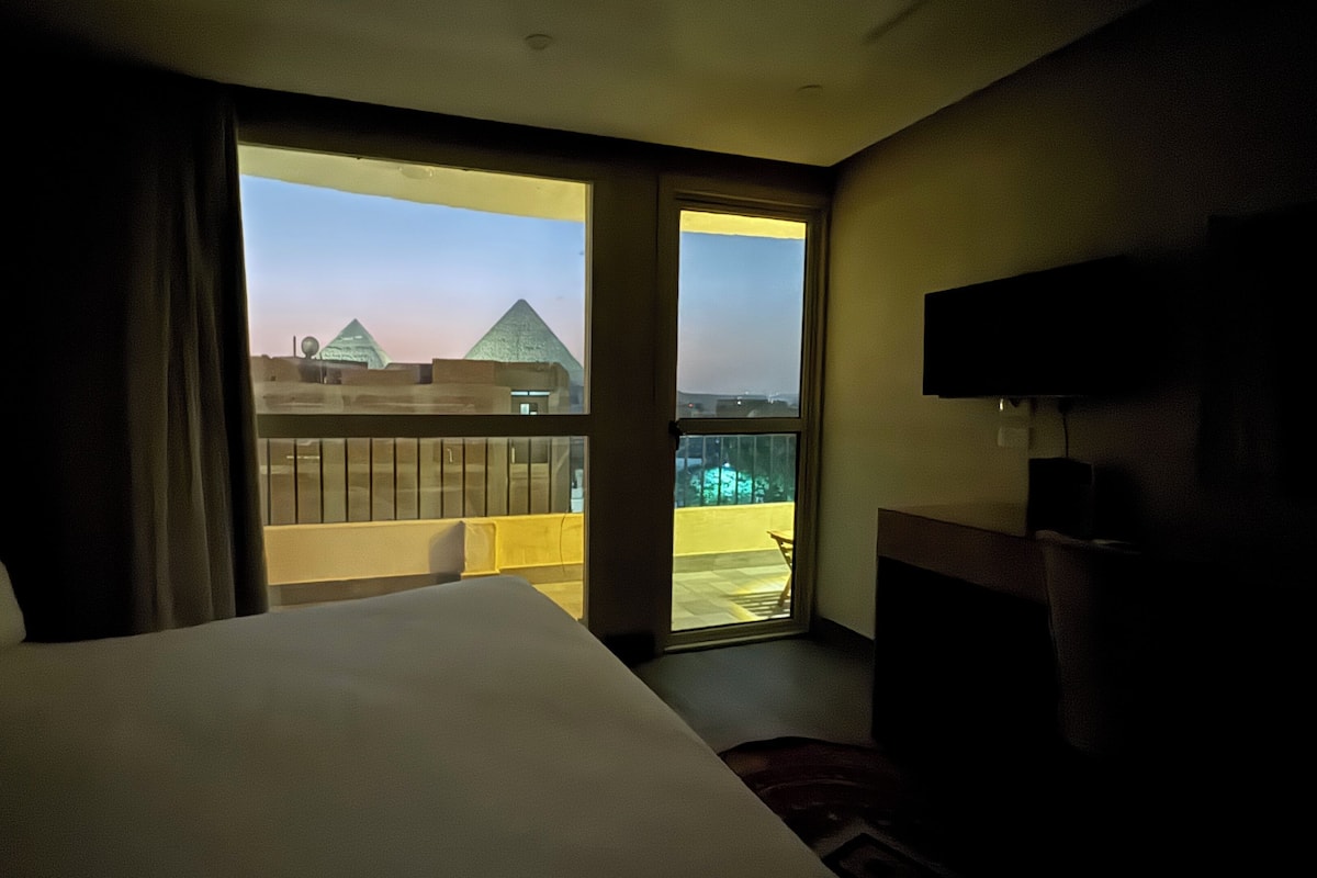 A hotel room with a bed, a TV, and a balcony with a view of buildings.