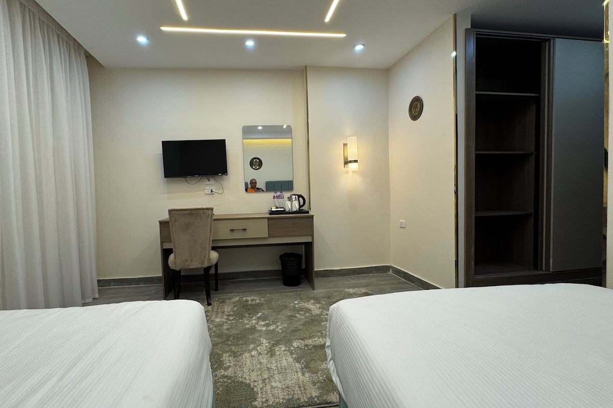 A hotel room with two beds, a desk with a chair, a TV, a mirror, and a wardrobe.