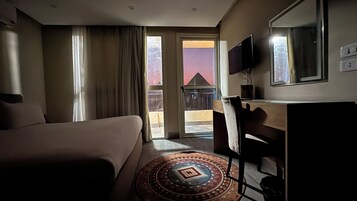 A hotel room with a bed, a desk, a chair, a TV, and a view of the outside.