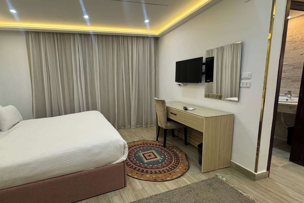 A bedroom with a bed, a desk, a chair, a TV, and a bathroom visible through an open door.