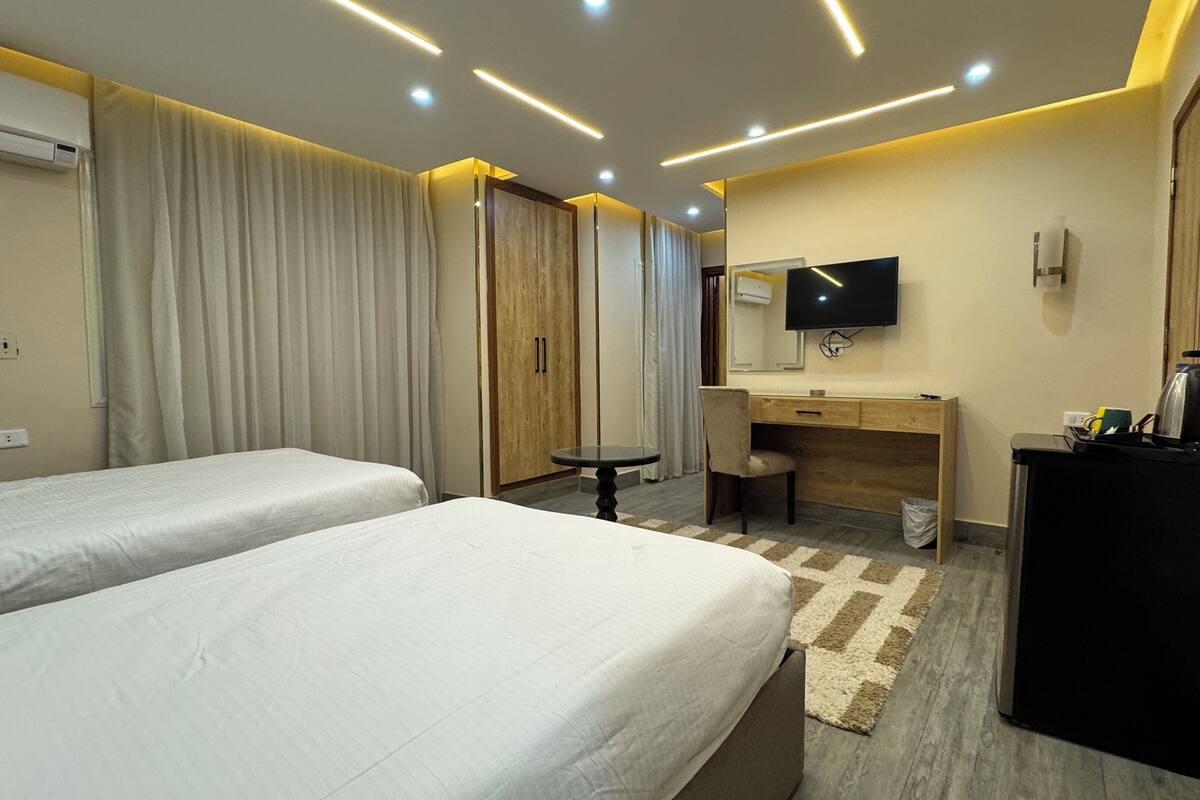A hotel room with two beds, a desk, a chair, a TV, and a coffee maker.