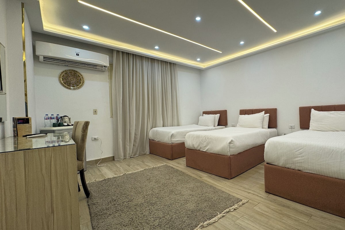A hotel room with two beds, a desk, and an air conditioning unit.