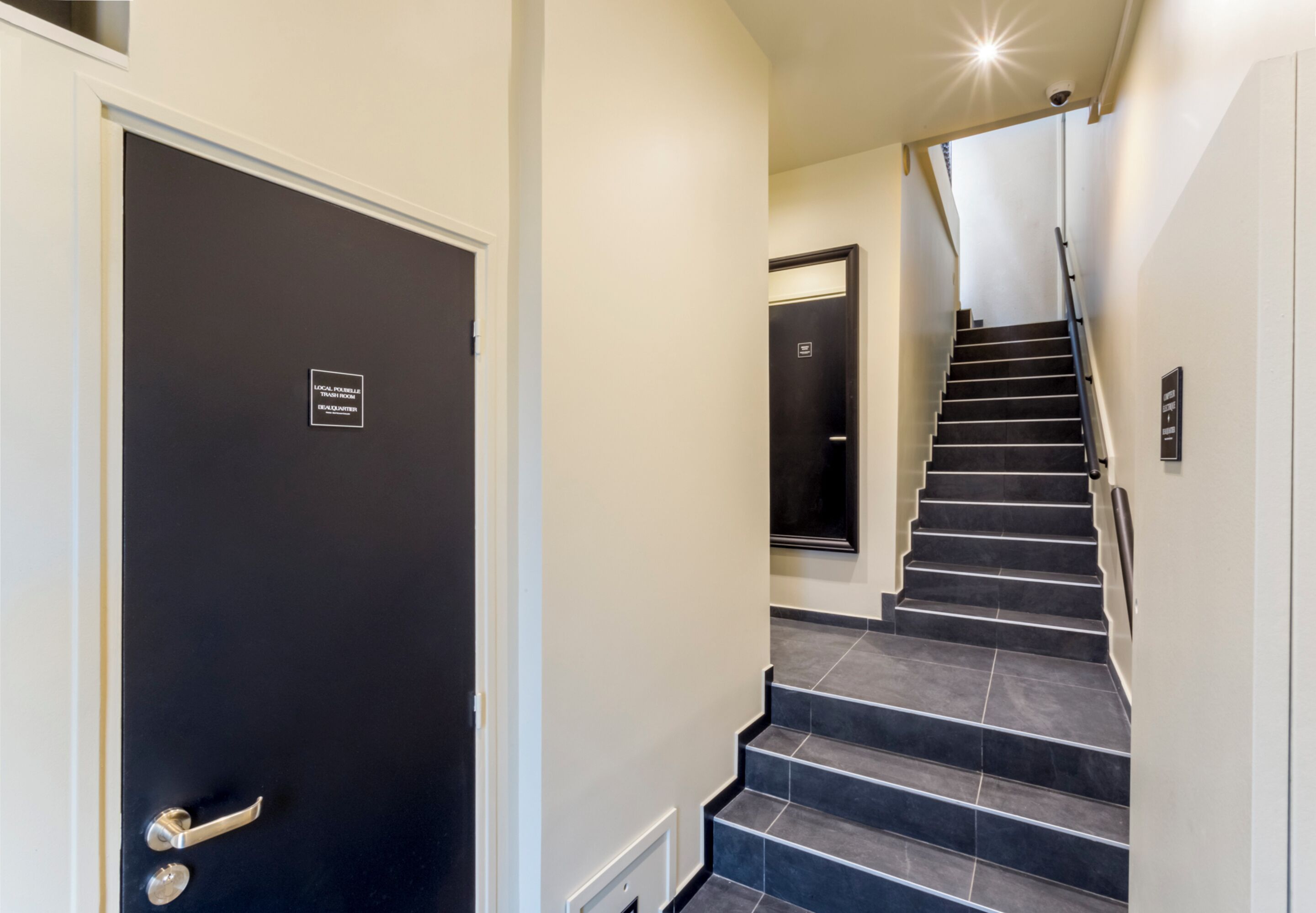 Un intérieur moderne avec une porte noire, un escalier aux marches sombres et un mur de couleur claire.