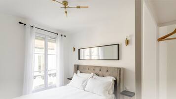 A bedroom with a large bed, a ceiling fan, a window with curtains, and a wall-mounted mirror.