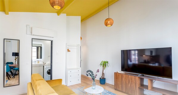 Un salon moderne comprenant un canapé, un téléviseur, un coin repas avec des chaises, une cuisine et une salle de bain.