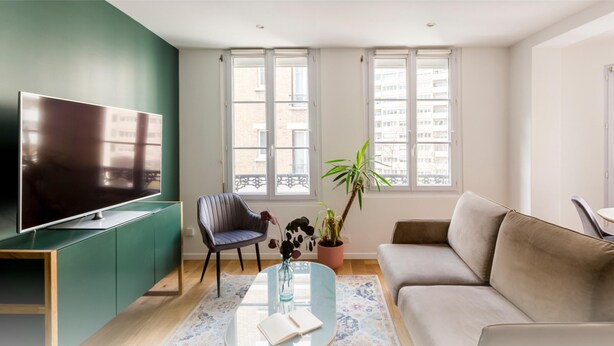 Una sala de estar moderna con una televisión de pantalla plana, un sofá, una silla, una mesa de centro y una planta en maceta.