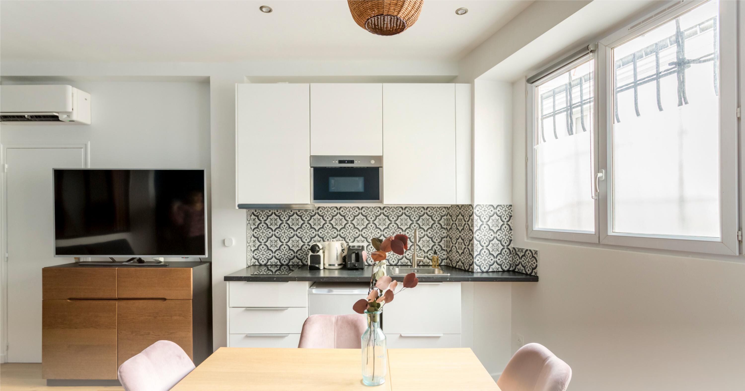 Una cocina moderna con gabinetes blancos, un salpicadero blanco y negro, un microondas y un ventanal grande.