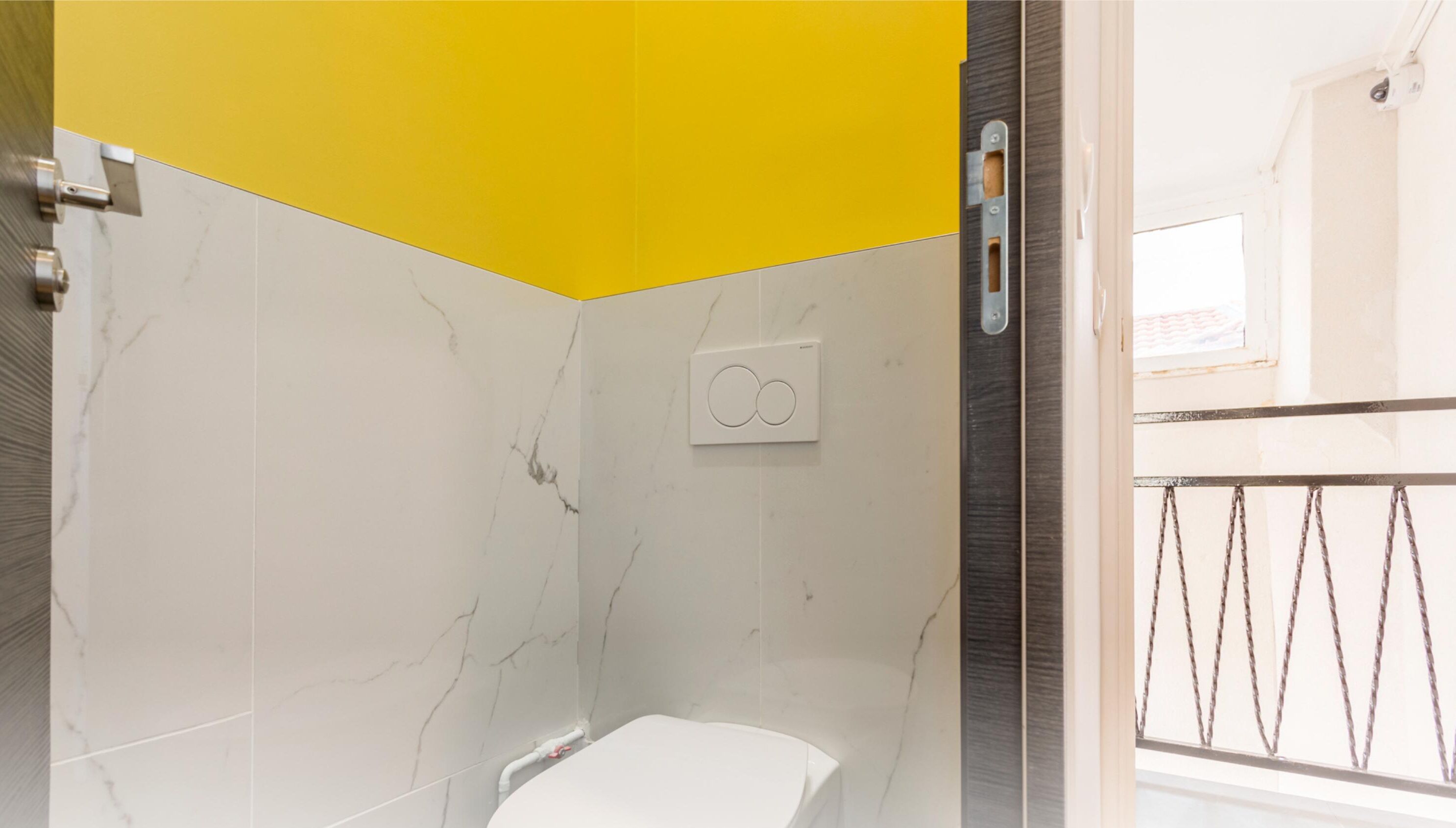 A bathroom with a white and yellow tiled wall, a white toilet, and a shower area with a metal door.