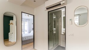 Una habitación de hotel moderna con cama, vestidor, zona de ducha y baño completo con inodoro y lavamanos.