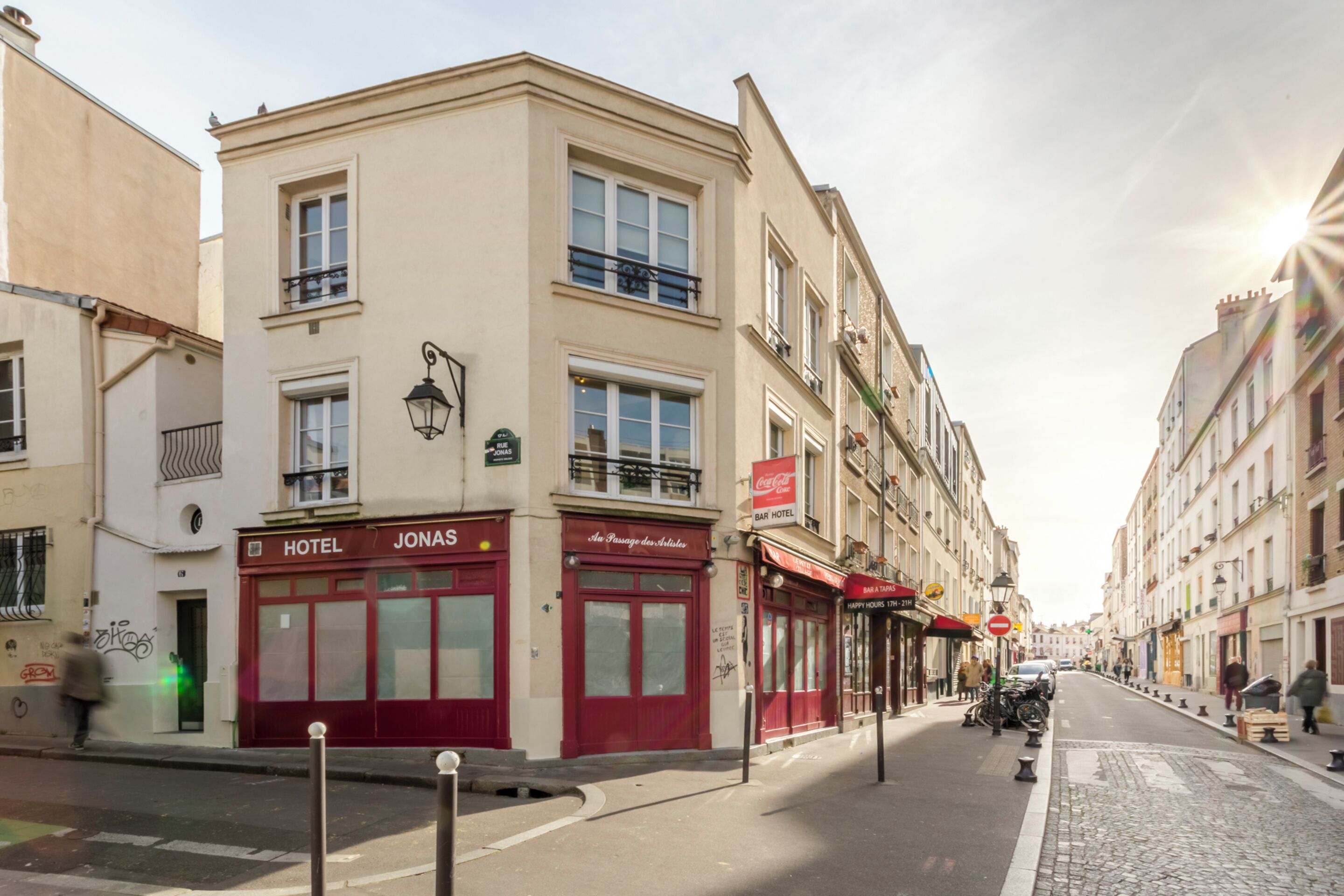 A hotel named "JONAS" with a red facade, a visible entrance, and a street view with cobblestone pavement and parked motorcycles.